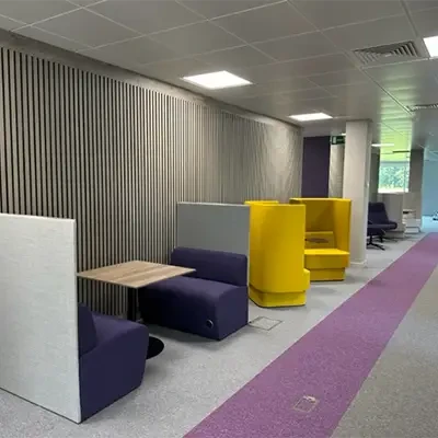 A photo of a hallway in a commercial building, with stylish yellow chairs, and a purple and gray flooring